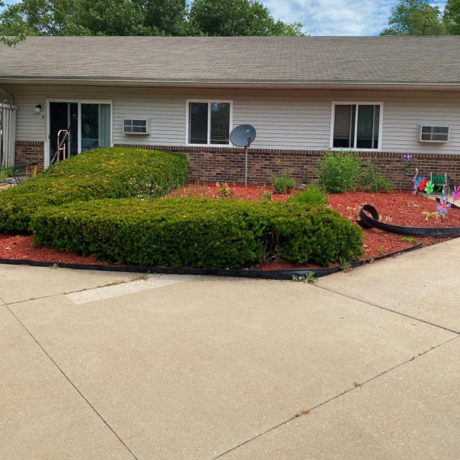 a yard with hedges and a house with a yard hose